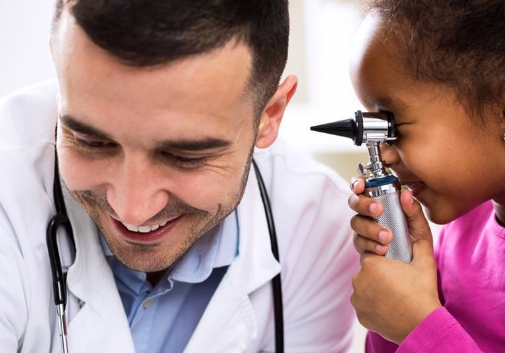 A laughing child holding a scope and pretending to look into a smiling doctor's ear.