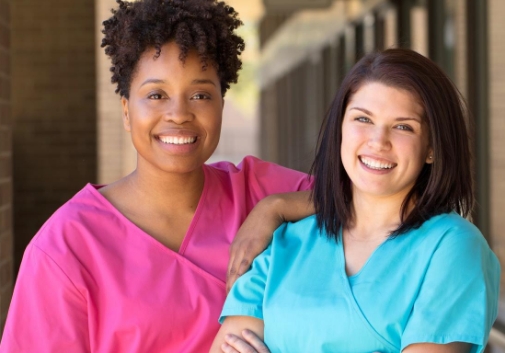 Two smiling nurses standing together in front of a medical facility 