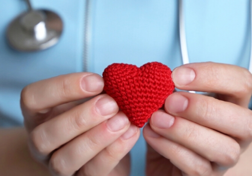 A nurse's hands holding a tiny red crochet heart