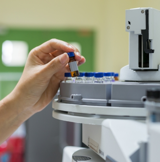 A hand loading a vial into a lab testing machine.