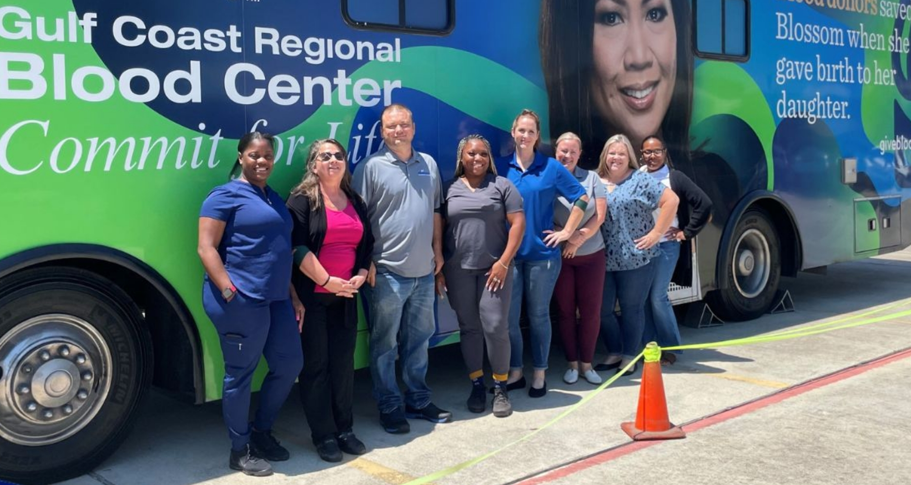 A group of employees standing together and smiling in front of a donation bus.